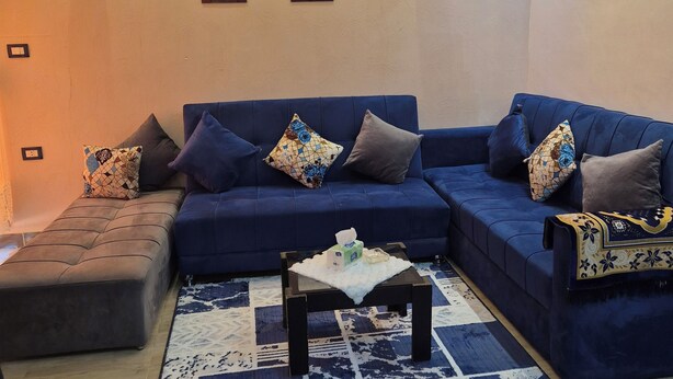 A living room with a blue sofa set, a patterned rug, and wall-mounted lights. - Star Apartment Hurghada (Hurghada)