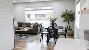 A modern living room with a sofa, round coffee table, and chairs. There is a large window providing a view of the outside.