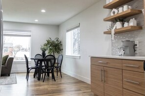 Una cocina moderna con armarios de madera, una zona de comedor con mesa y sillas, y un ventanal que proporciona luz natural.