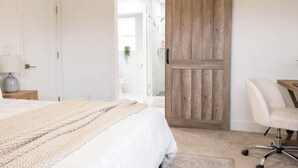 A bedroom with a large bed, a wooden door, a desk, and a chair.