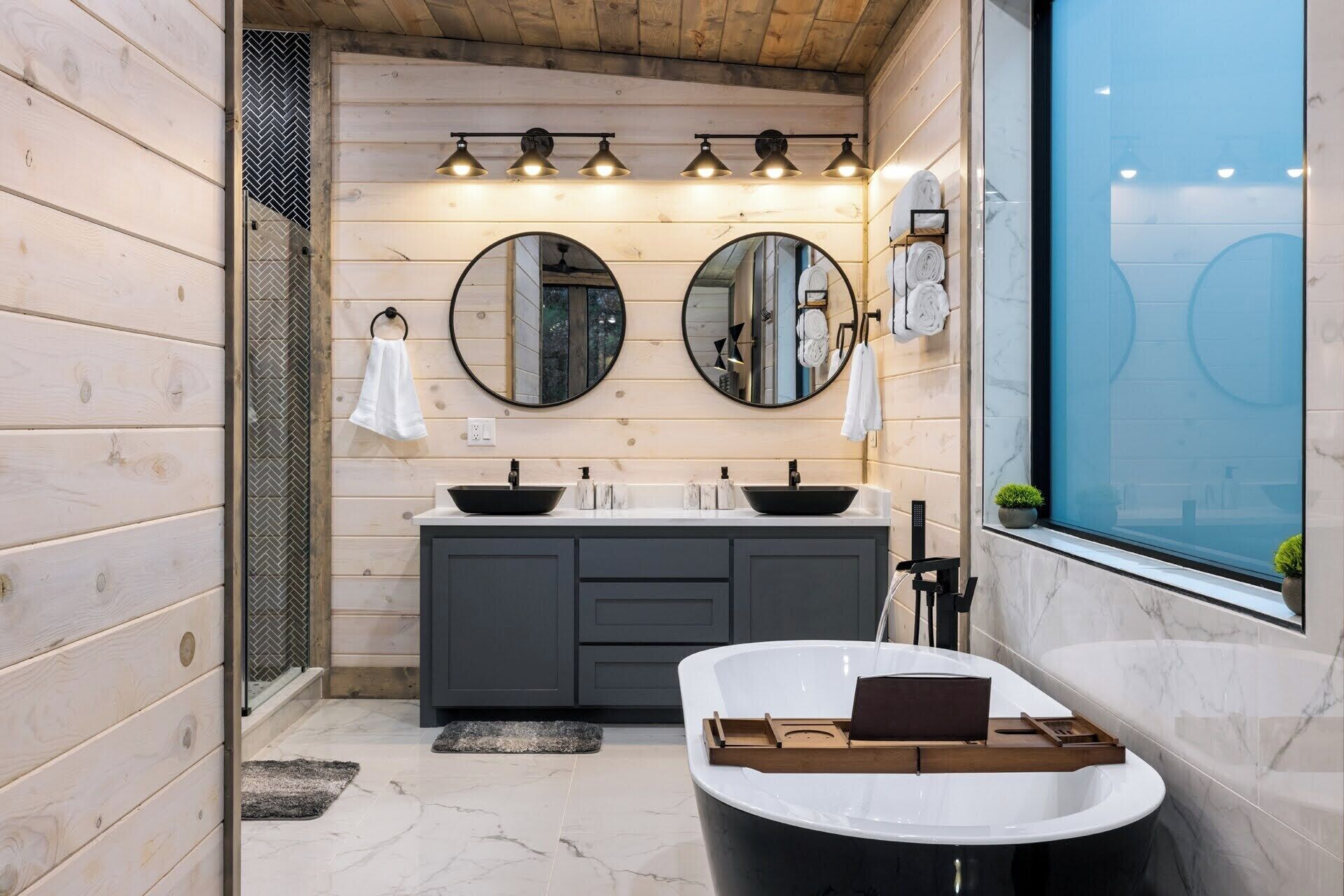Ein modernes Badezimmer mit Holzpaneelen, einer freistehenden Badewanne, zwei Waschbecken und großen Spiegeln.