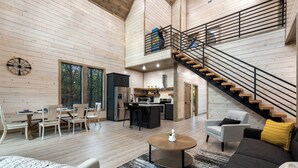 A spacious living area with a kitchen, dining table, and a staircase leading to an upper level. - In the Pines: Eco Retreat heated Pool, Hot Tub & Games (Broken Bow)