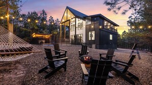 A modern house with a deck, outdoor seating, and a fire pit. - In the Pines: Eco Retreat heated Pool, Hot Tub & Games (Broken Bow)