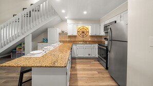 A modern kitchen with white cabinets, a granite countertop, stainless steel appliances, and a wooden staircase.