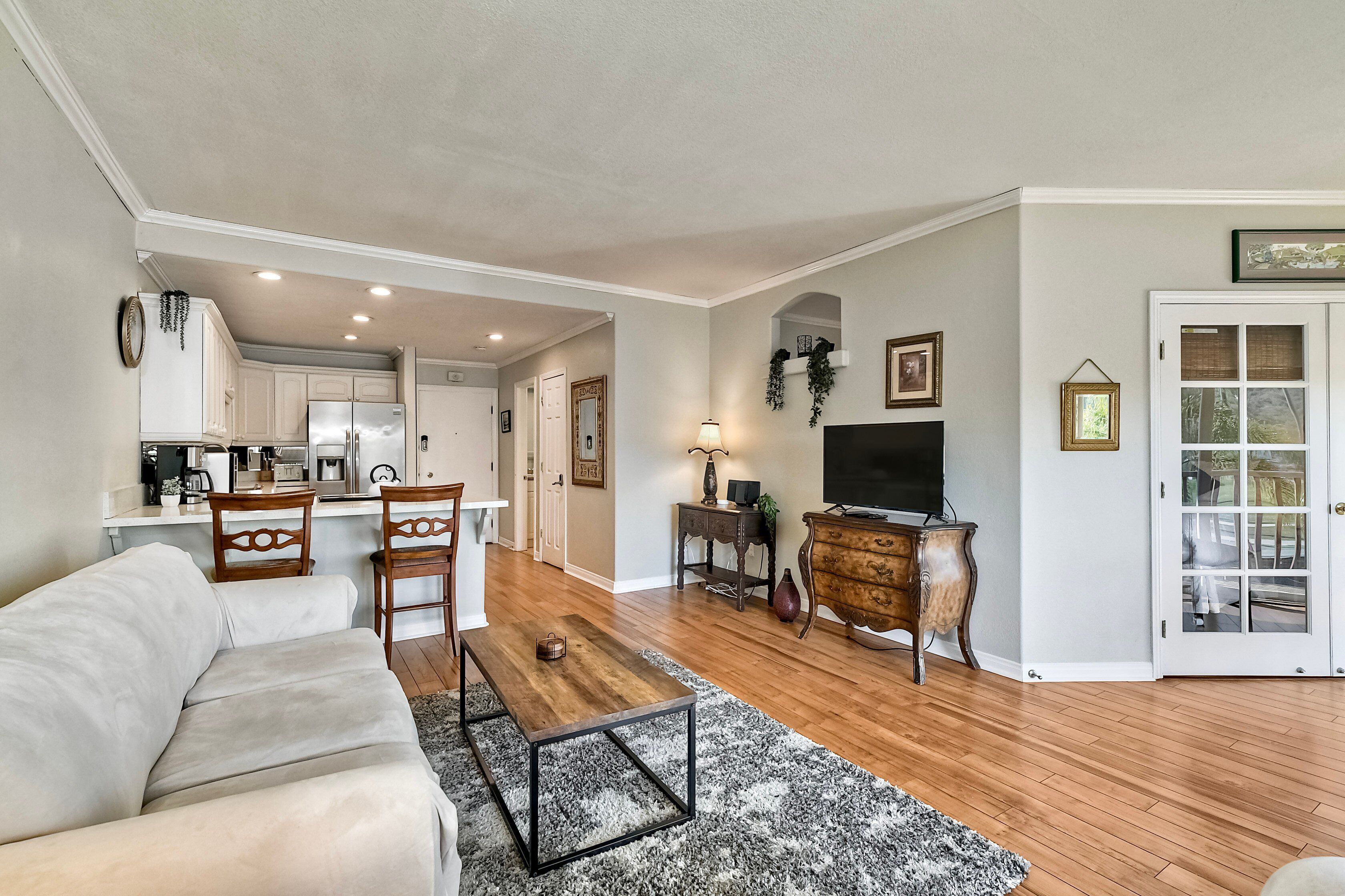 A living room with a sofa, a coffee table, a TV, and a kitchen in the background.