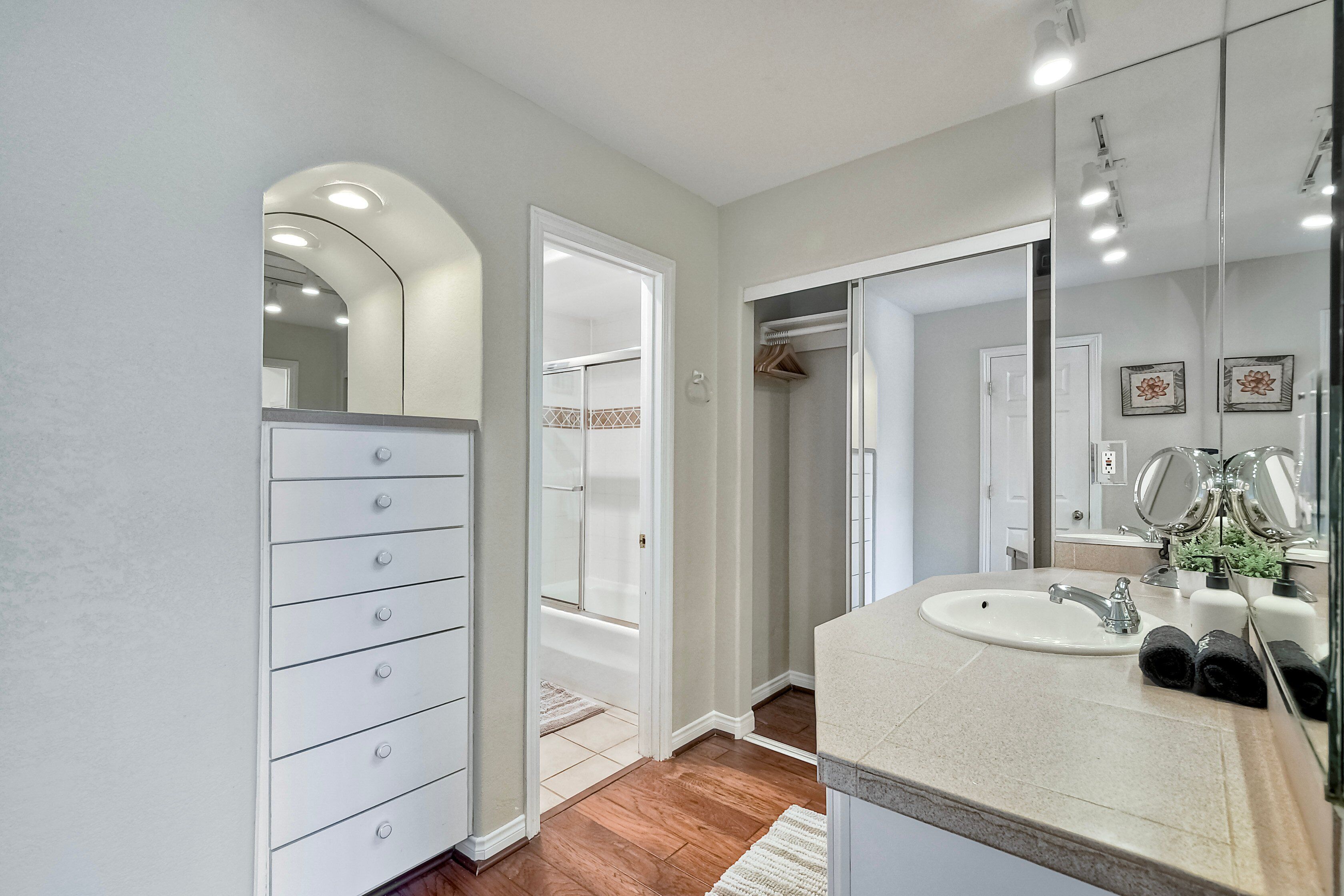 A modern bathroom with a white vanity, a large mirror, and a walk-in closet.