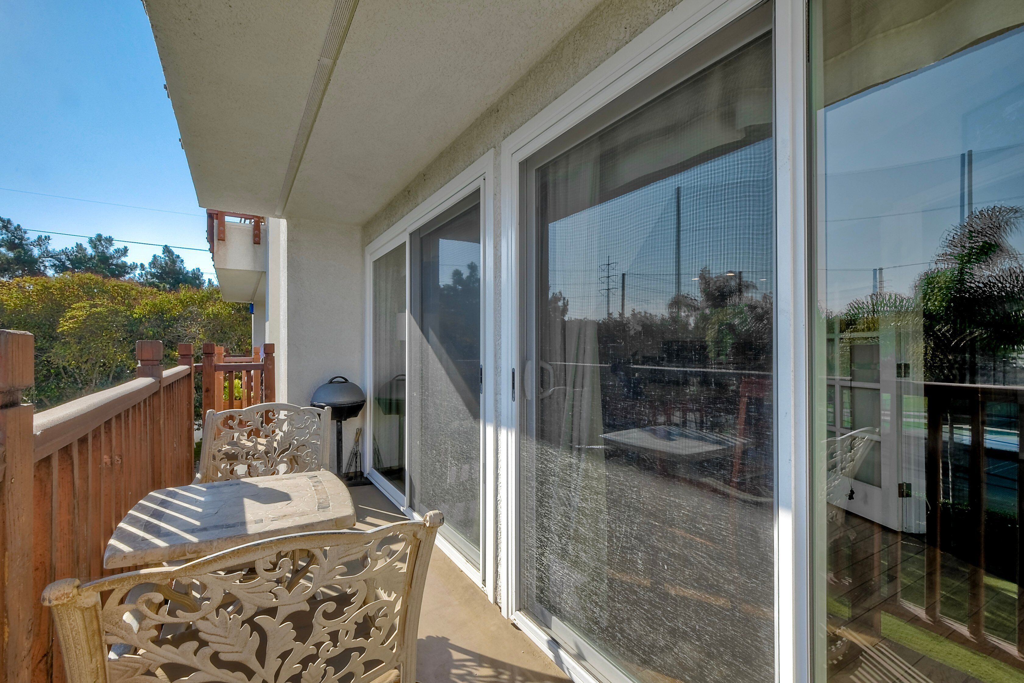 A balcony with a wooden chair and table, large sliding glass doors, and a view of a garden.