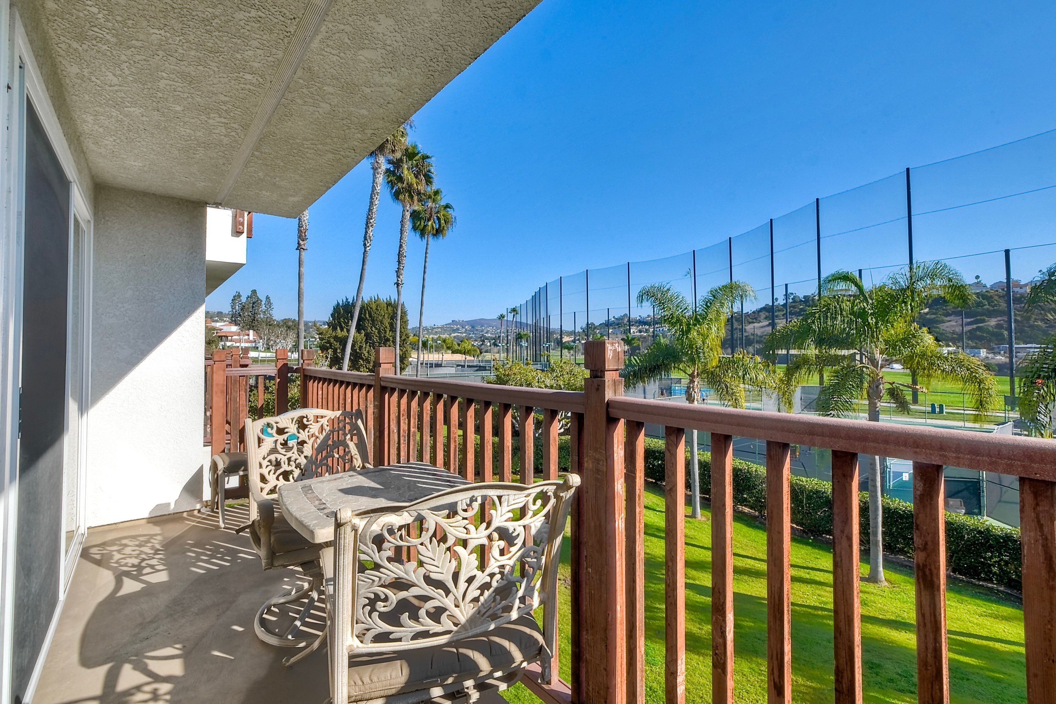 Un balcon avec une table et des chaises, une vue sur un paysage verdoyant et un ciel bleu dégagé.