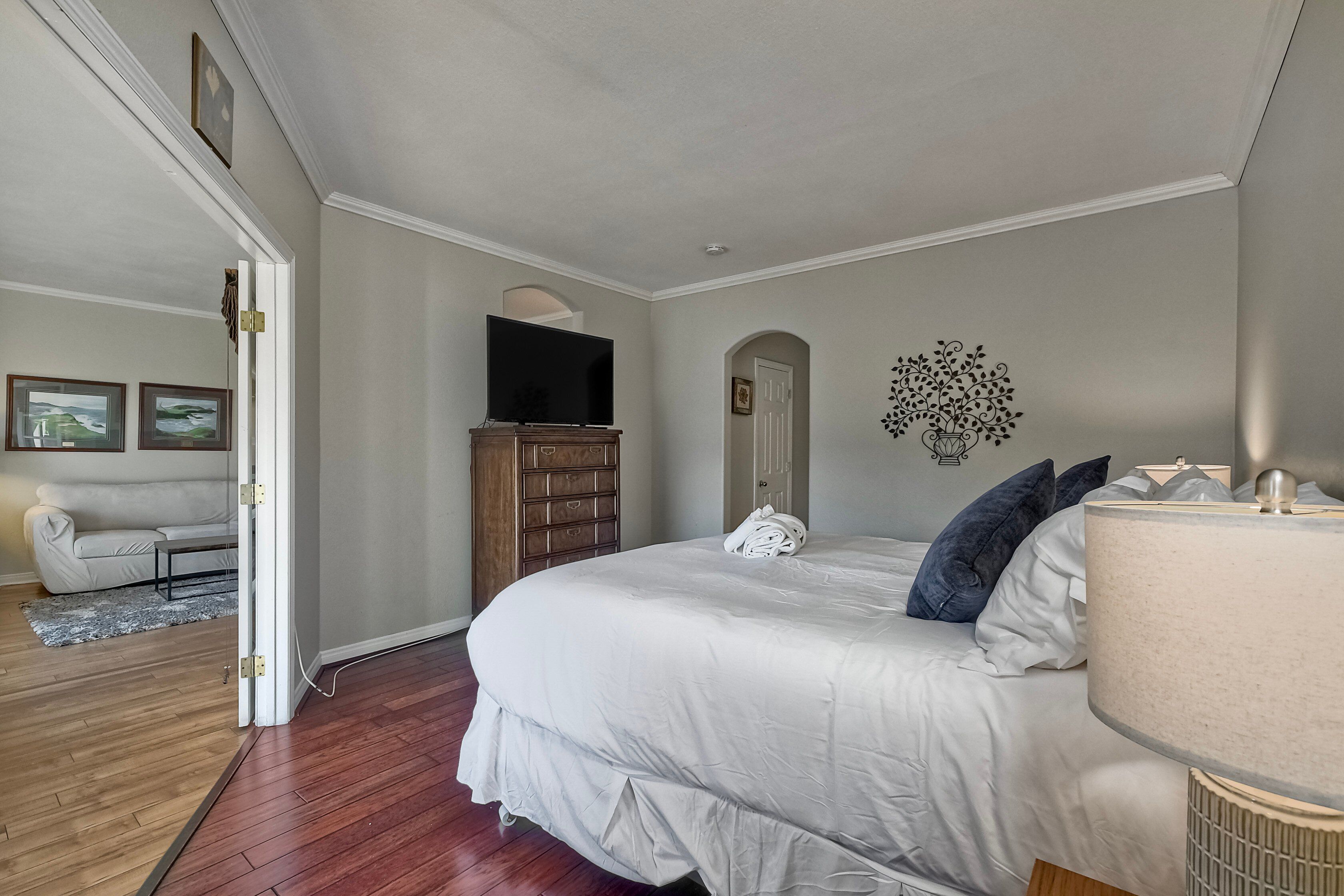 A bedroom with a large bed, a TV, a dresser, and a door leading to another room.
