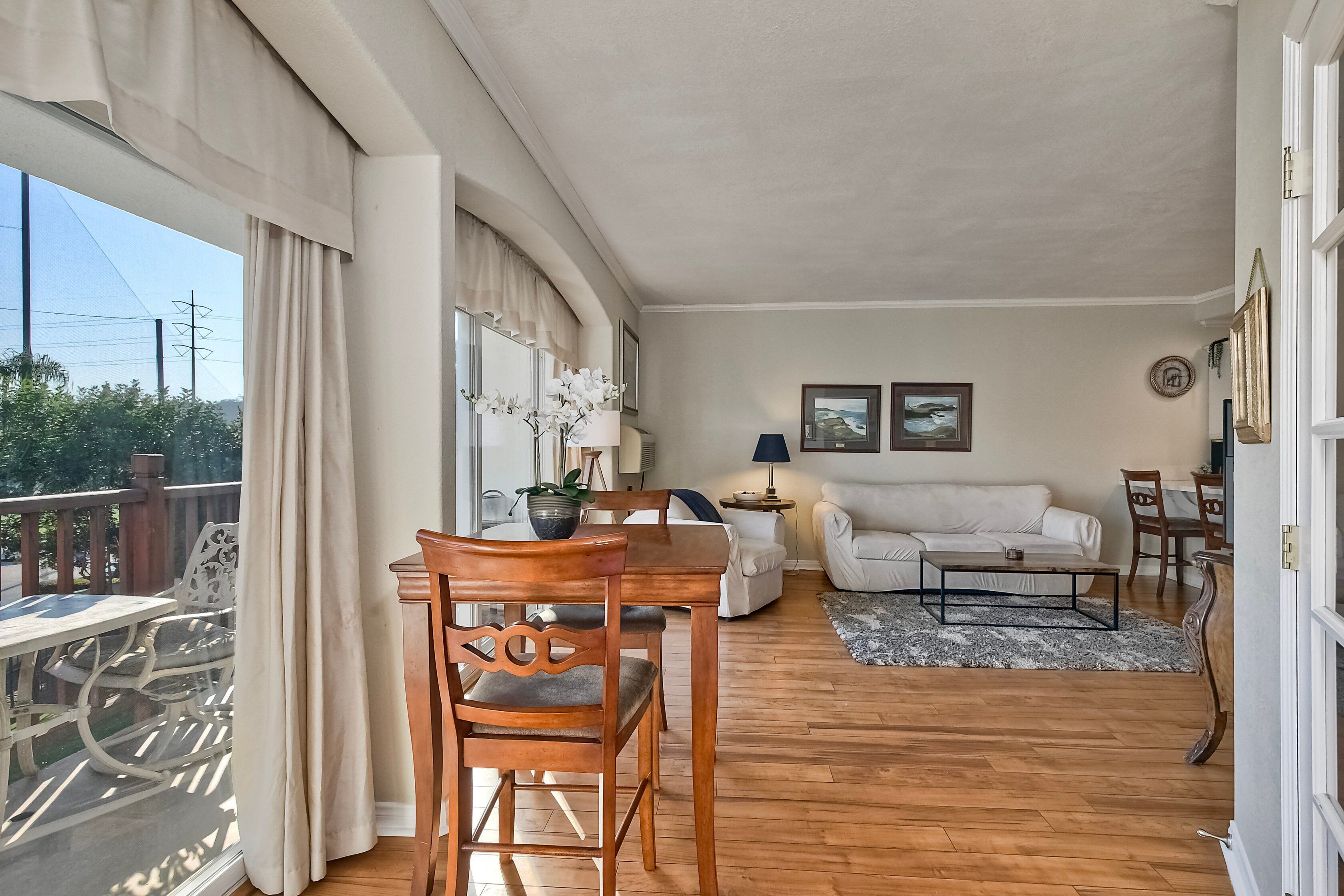 Una sala de estar con una mesa de comedor de madera, sofá blanco y un balcón con vistas al exterior.