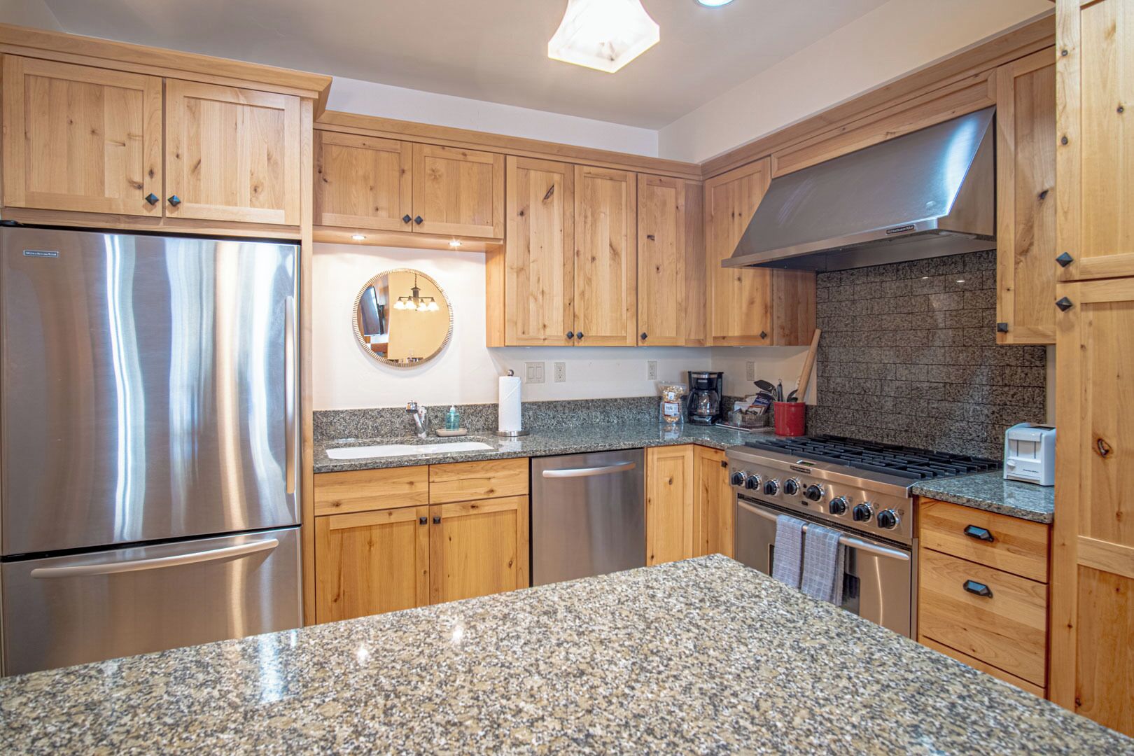 A modern kitchen with wooden cabinets, stainless steel appliances, granite countertops, and a central island.