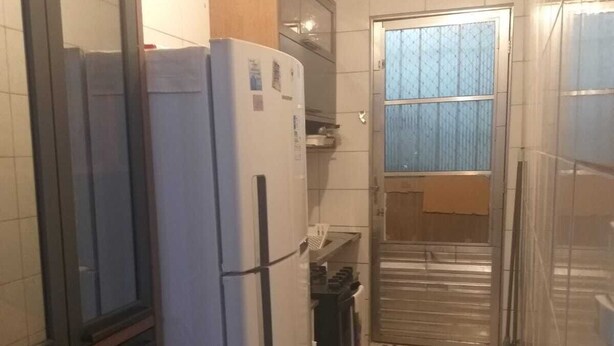 Een compacte keuken met een koelkast, een klein spoelgedeelte en een raam met zonwering.