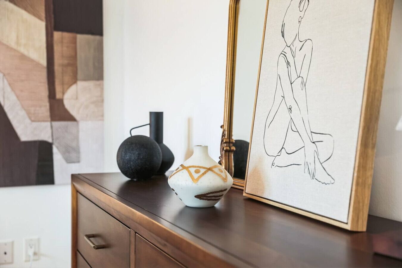 A wooden dresser with a vase, a framed drawing, and two black vases.