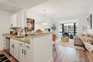 A modern kitchen with white cabinets, a granite countertop, and a dining area with a round coffee table. - Elegant Urban Living Downtown Stamford (Stamford)