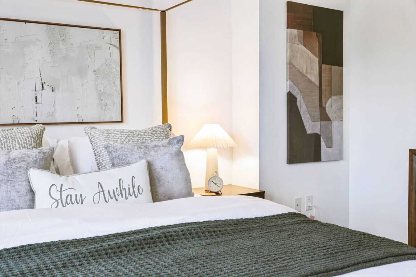 A neatly arranged bedroom with a bed, pillows, a bedside lamp, and wall art.