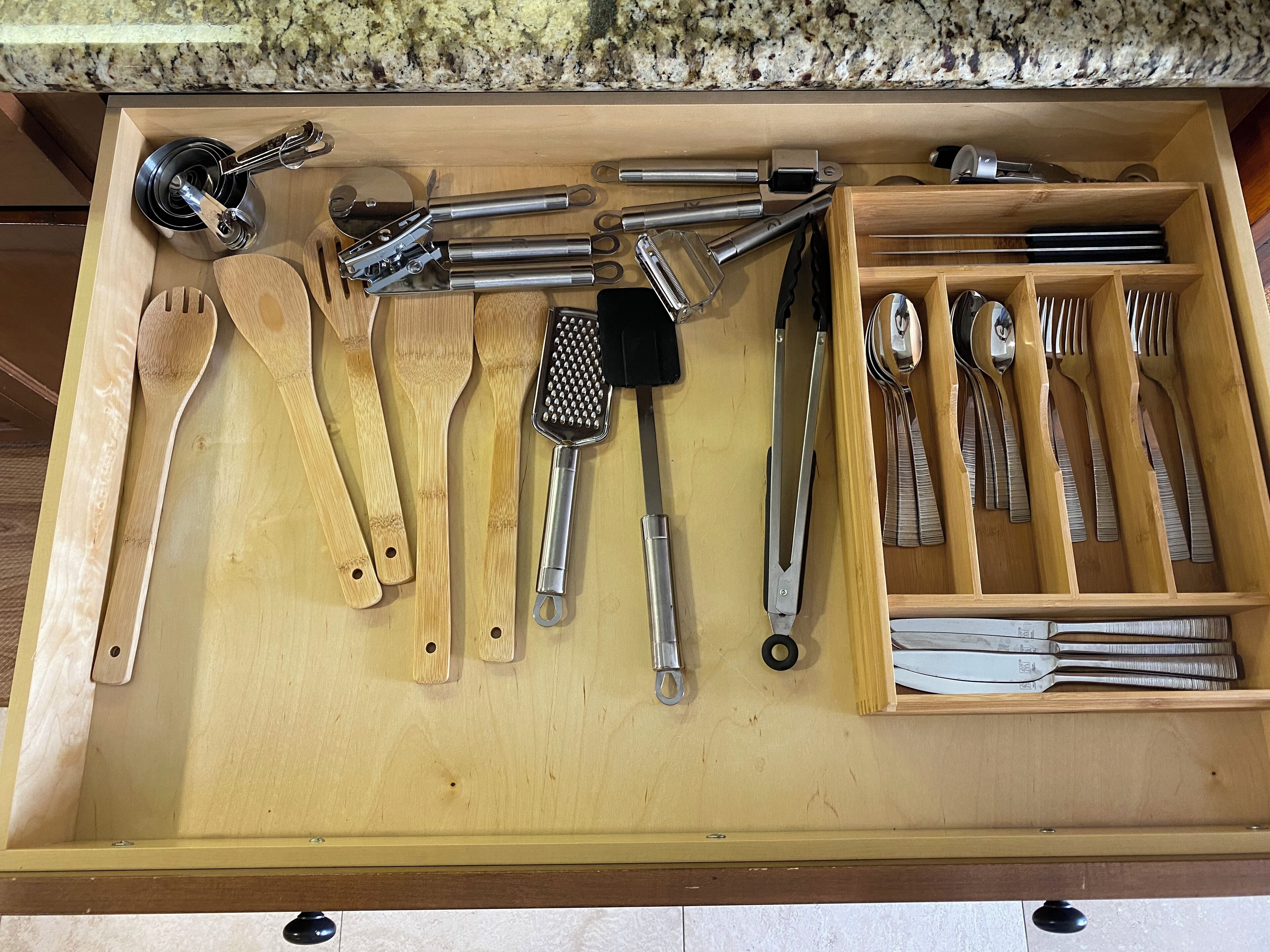 A drawer with various kitchen utensils including wooden spoons, spatulas, tongs, and a grater.