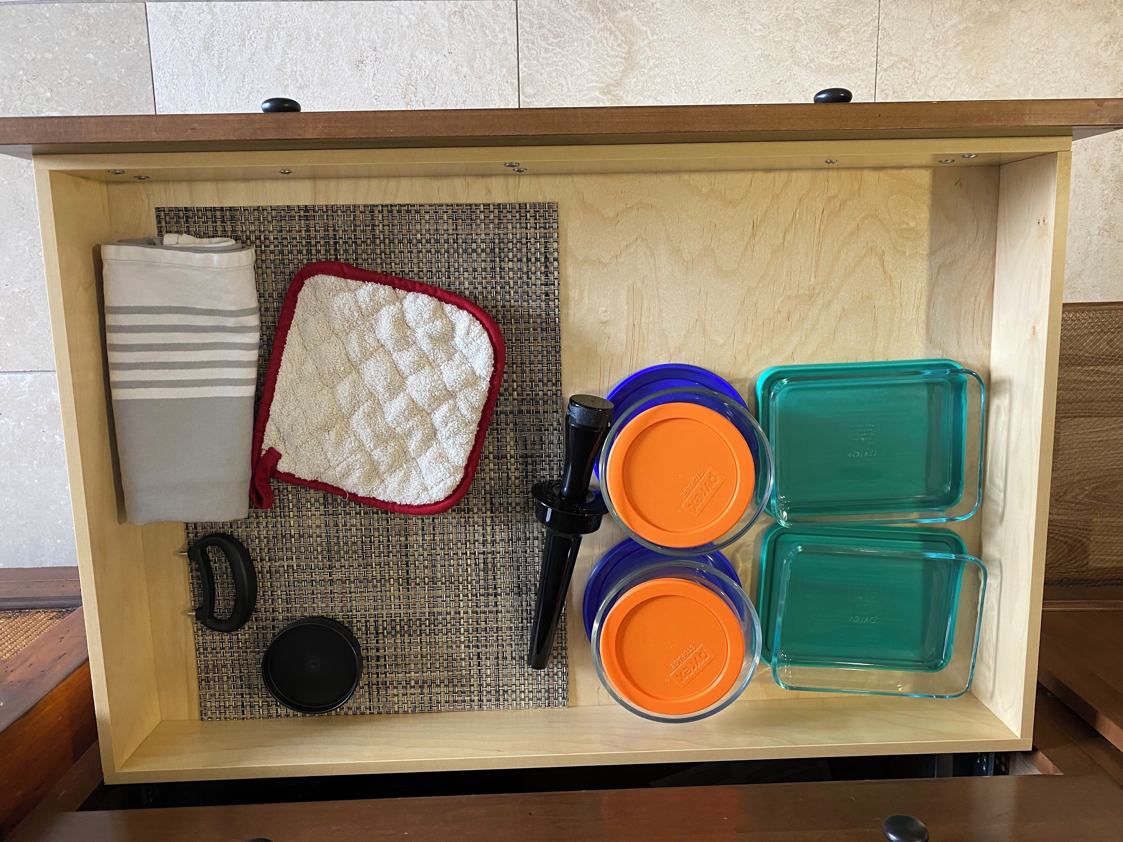 A storage box with a woven mat, a white cushion, a black object, and two containers with orange lids.