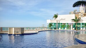 A swimming pool with a view of the ocean and a building with palm trees. - In bocagrande and luxurious apartment in Cartagena (Cartagena de Indias)