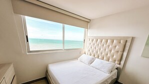 A bedroom with a large window, a tufted headboard, and a bed with white linens. - In bocagrande and luxurious apartment in Cartagena (Cartagena de Indias)