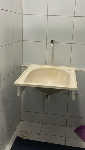 A small, white, rectangular sink with a drainpipe, mounted on a tiled wall in a corner.