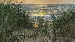 A beach scene with sand and grass in the foreground, and a sunset in the background. - OCEANVIEW CONDO:
Outer Banks Oceanside cozy 2-bedroom condo in Kill Devil Hills. (Kill Devil Hills)