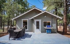 A small cabin with a deck, outdoor seating, and a grill.