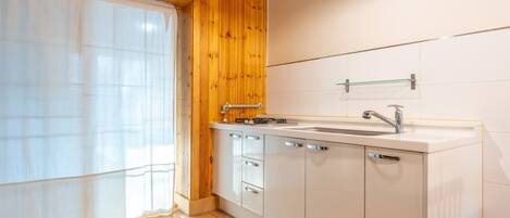 A kitchen with wooden walls, a white countertop, a sink, and a window with a sheer curtain.