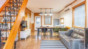 A modern living room with a wooden staircase, a dining area, and a kitchen.