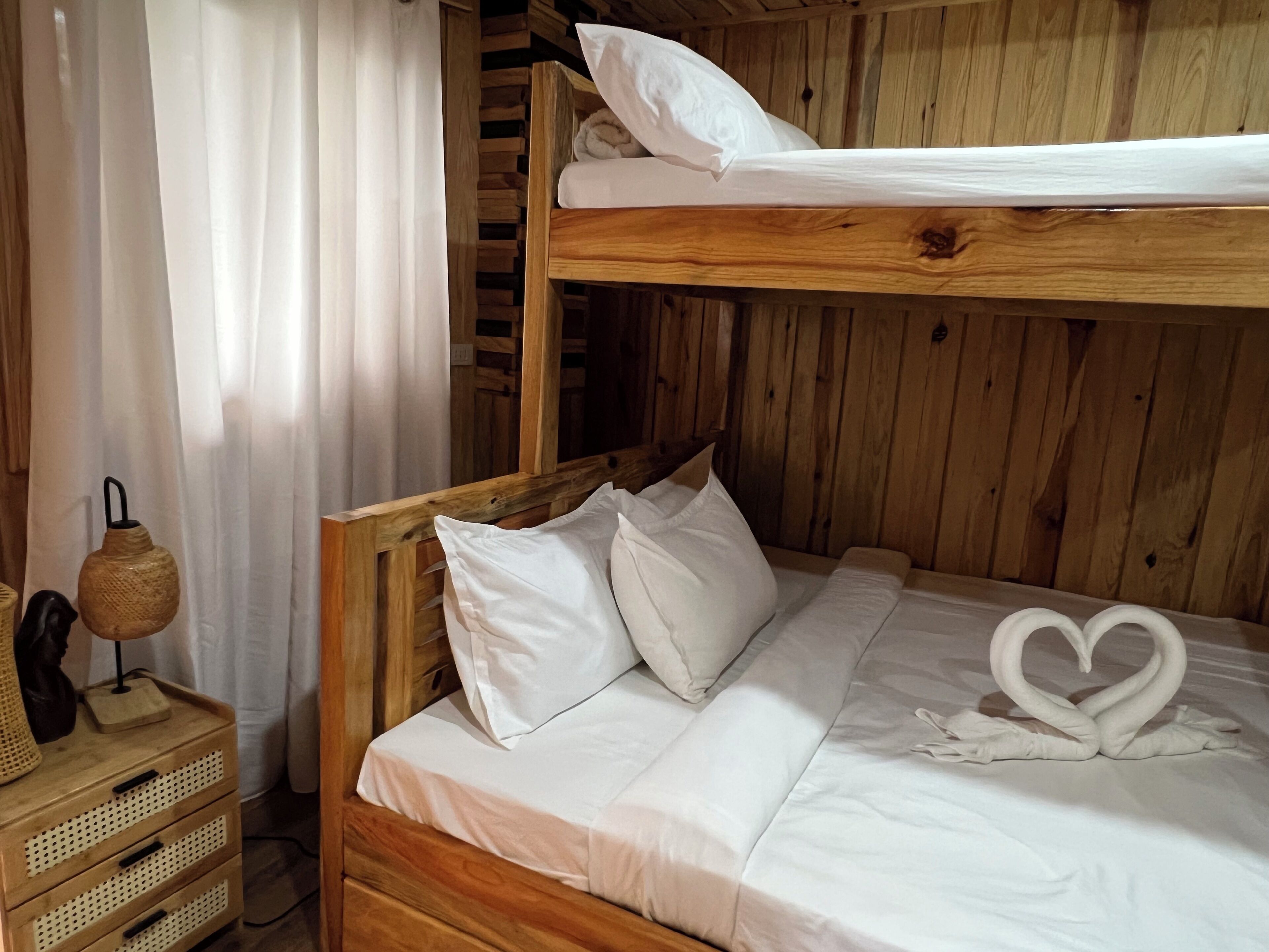 Ein Stockbett mit weißer Bettwäsche und Kissen, ein gewebter Korb und ein herzförmiges Handtuch auf dem unteren Bett.