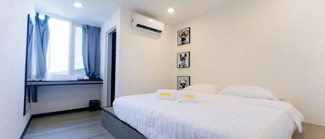 Une chambre d’hôtel moderne avec un grand lit, une fenêtre avec des rideaux, un appareil de climatisation et des tableaux encadrés au mur.