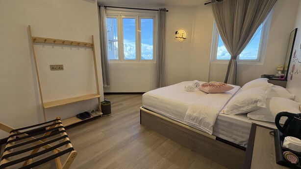 A bedroom with a bed, a wooden chair, a bedside table with a phone, and a window with curtains. - Ru Jia Hai She Hotel (Semporna)