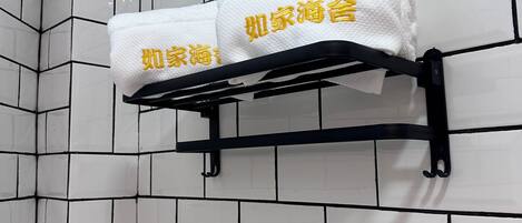 A bathroom with white tiled walls and a black towel rack holding two white towels with yellow text.