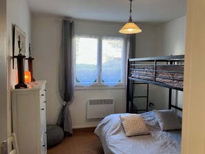 Un dormitorio con una cama nido, una ventana con cortinas, un calentador y una lámpara de noche.
