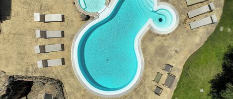 An aerial view of a swimming pool with a unique shape, surrounded by lounge chairs and a small hot tub.