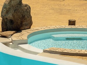 A swimming pool with clear water, surrounded by stone tiles and a large rock. - Villa Sandalia with private pool and jacuzzi (Olbia)