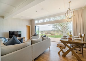 Een moderne woonkamer met een grote bank, een eettafel voor vier personen en een televisie op een standaard.
