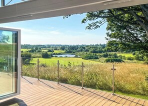 A modern building with a glass balcony overlooking a lush landscape with a lake.