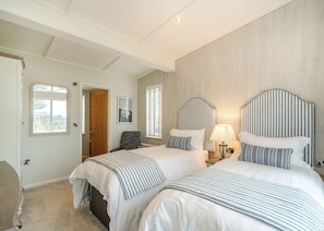 Een hotelkamer met twee bedden, een stoel, een lamp en een deur naar een andere kamer.