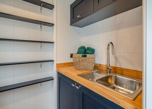 A kitchen with white cabinets, a wooden countertop, a stainless steel sink, and a basket with towels.