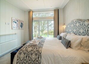 A bedroom with a large bed, a view of the outdoors, and artwork on the wall.