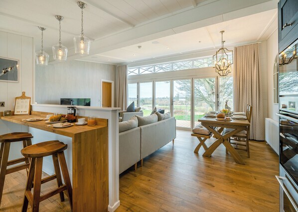 A modern kitchen with a wooden island, bar stools, a sofa, and a dining table with chairs.