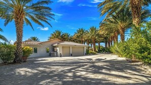 A residential property with a paved driveway, a garage, and palm trees. - PalmSpring Luxury Vacation Home-Salted Pool & Spa. (Thousand Palms)