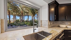 A modern kitchen with a large window, dark cabinetry, and a marble countertop. - PalmSpring Luxury Vacation Home-Salted Pool & Spa. (Thousand Palms)