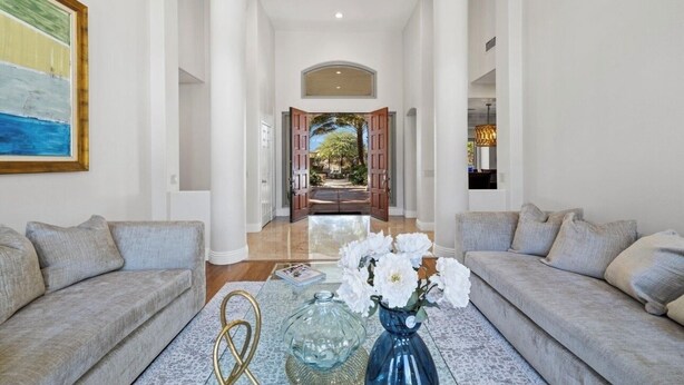 A spacious living area with a large painting on the wall, a sofa, a coffee table with decorative items, and a view into the dining area through an open door. - PalmSpring Luxury Vacation Home-Salted Pool & Spa. (Thousand Palms)