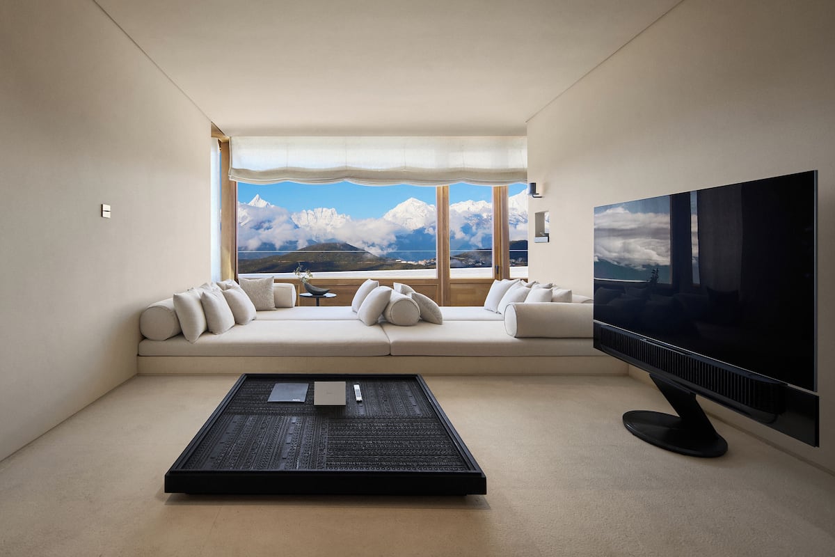 Un salon moderne doté d’un grand téléviseur, d’un ensemble de canapés et offrant une vue sur les montagnes grâce à de grandes fenêtres.