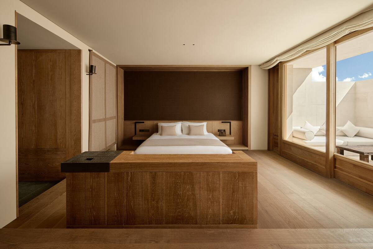 Une chambre à coucher moderne avec un grand lit, une tête de lit en bois et un banc intégré au pied du lit.