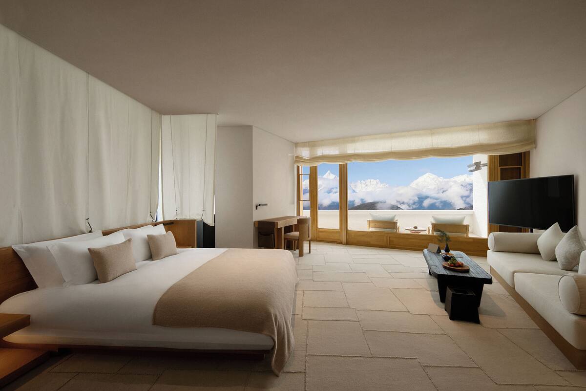 Une chambre d’hôtel moderne, dotée d’un grand lit, d’un canapé, d’un bureau et d’une télévision. La chambre dispose d’une grande fenêtre offrant une vue sur les montagnes.