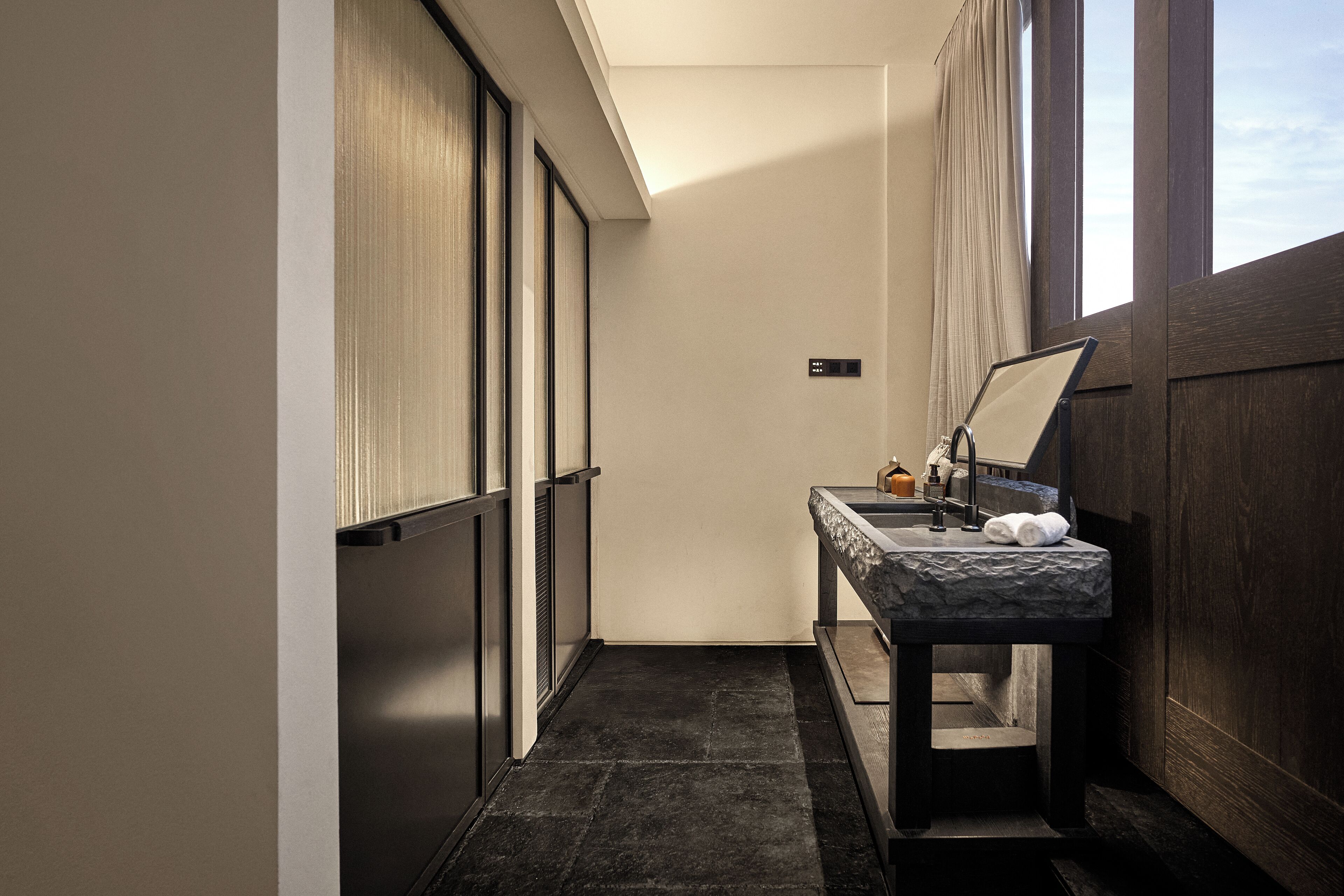 Une petite salle de bain avec un sol carrelé foncé, un lavabo surmonté d’un plan de travail en marbre et un miroir.