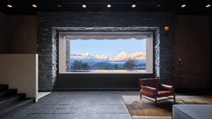 Habitación con una ventana grande que ofrece vistas a la montaña, un sillón de cuero y una pared de piedra.