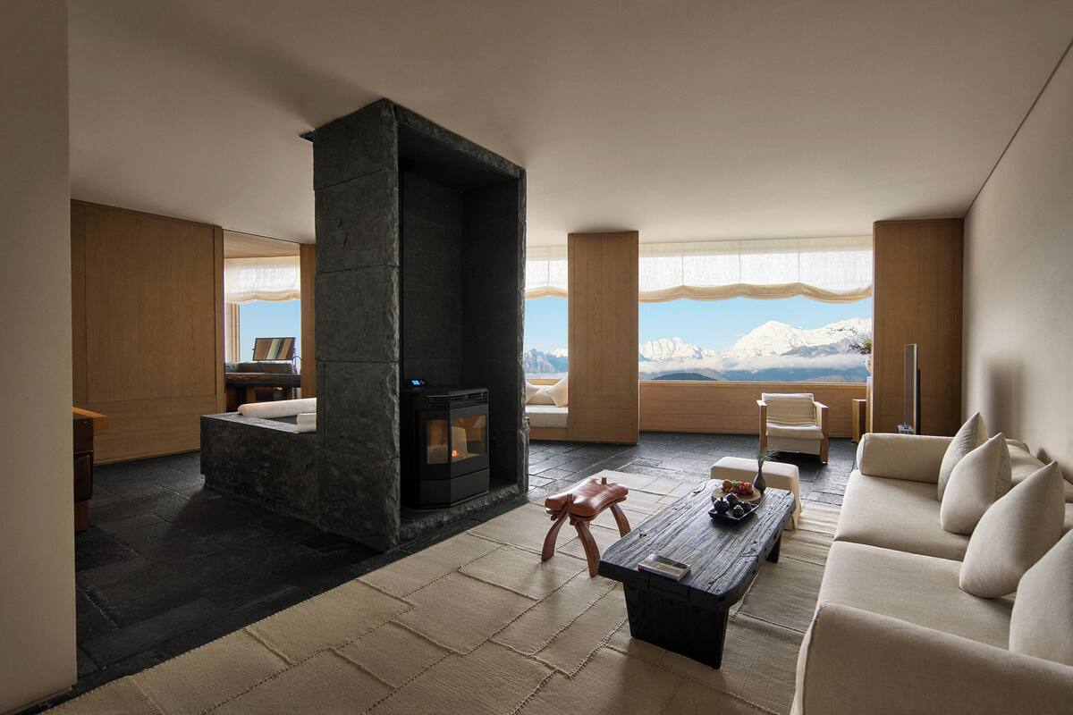 Un salon moderne avec une cheminée en pierre, un canapé, une table basse et une vue sur les montagnes grâce à de grandes fenêtres.